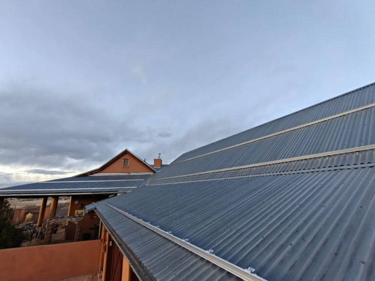 Metal corrugated roofs and a brown house under a clear, slightly cloudy sky, with the photo taken at an angle highlighting the rooflines.
