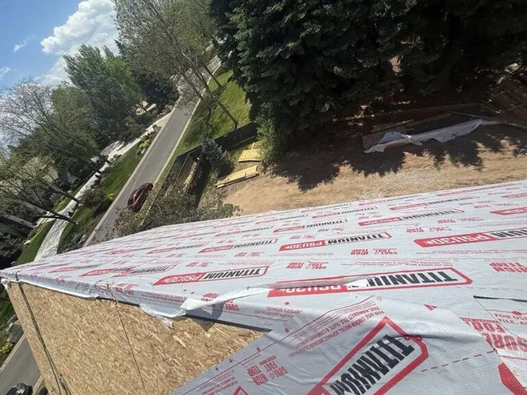 View from a rooftop under construction, covered with Owens Corning roofing underlayment; trees, street, and yard are visible in the background on a sunny day.