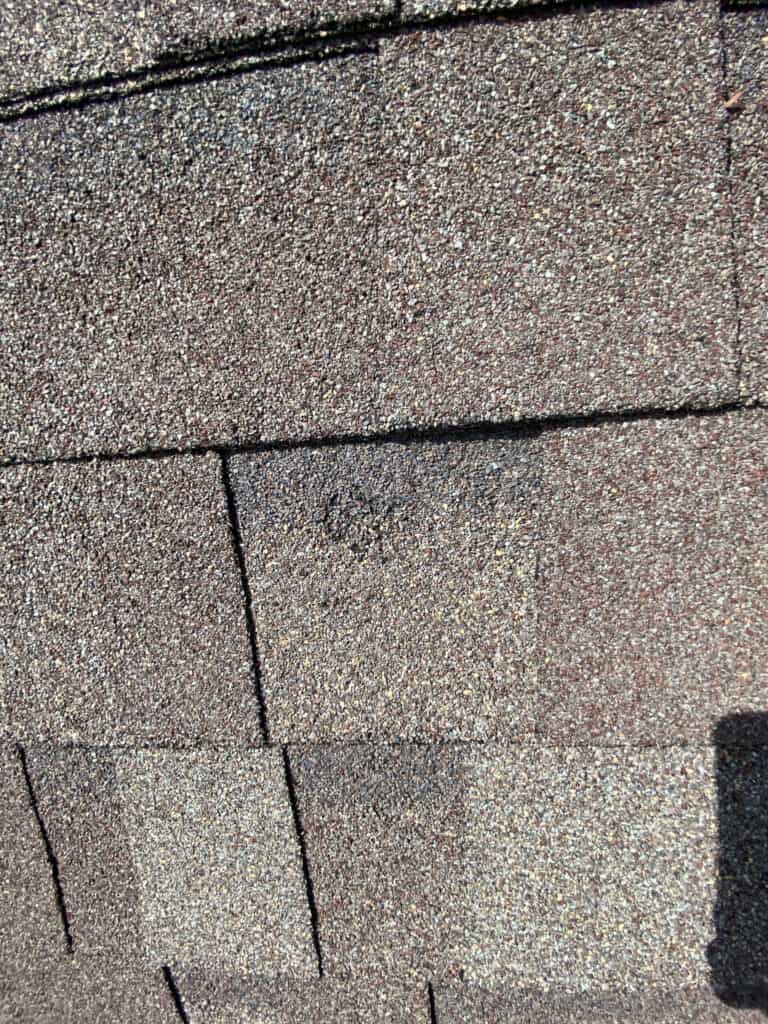 Close-up of brown asphalt roof shingles, showing their rough, grainy texture and overlapping arrangement in rows under sunlight.